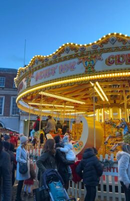 There is a queue of woman and children waiting at an illuminated MerryGoRound in the Dublin Castle Christmas Market